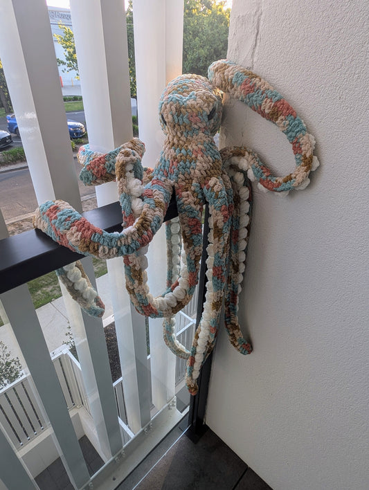 giant crochet octopus handmade sitting on black balcony ledge looking like he is trying to escape